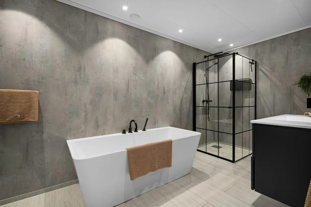 Modern bathroom with freestanding bath, textured grey tiles and black framed shower screen
