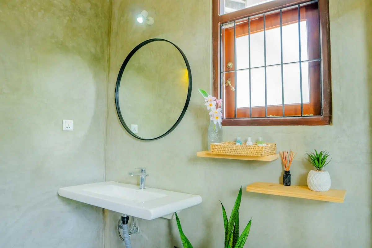 Compact bathroom with green concrete finish, round mirror, floating basin and natural light
