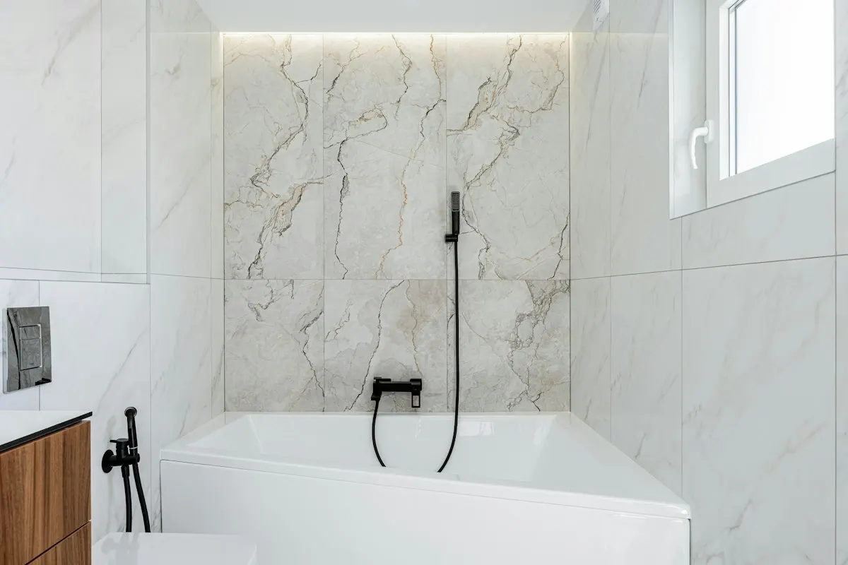 Bright luxury bathroom with marble walls, freestanding white bathtub and black tapware
