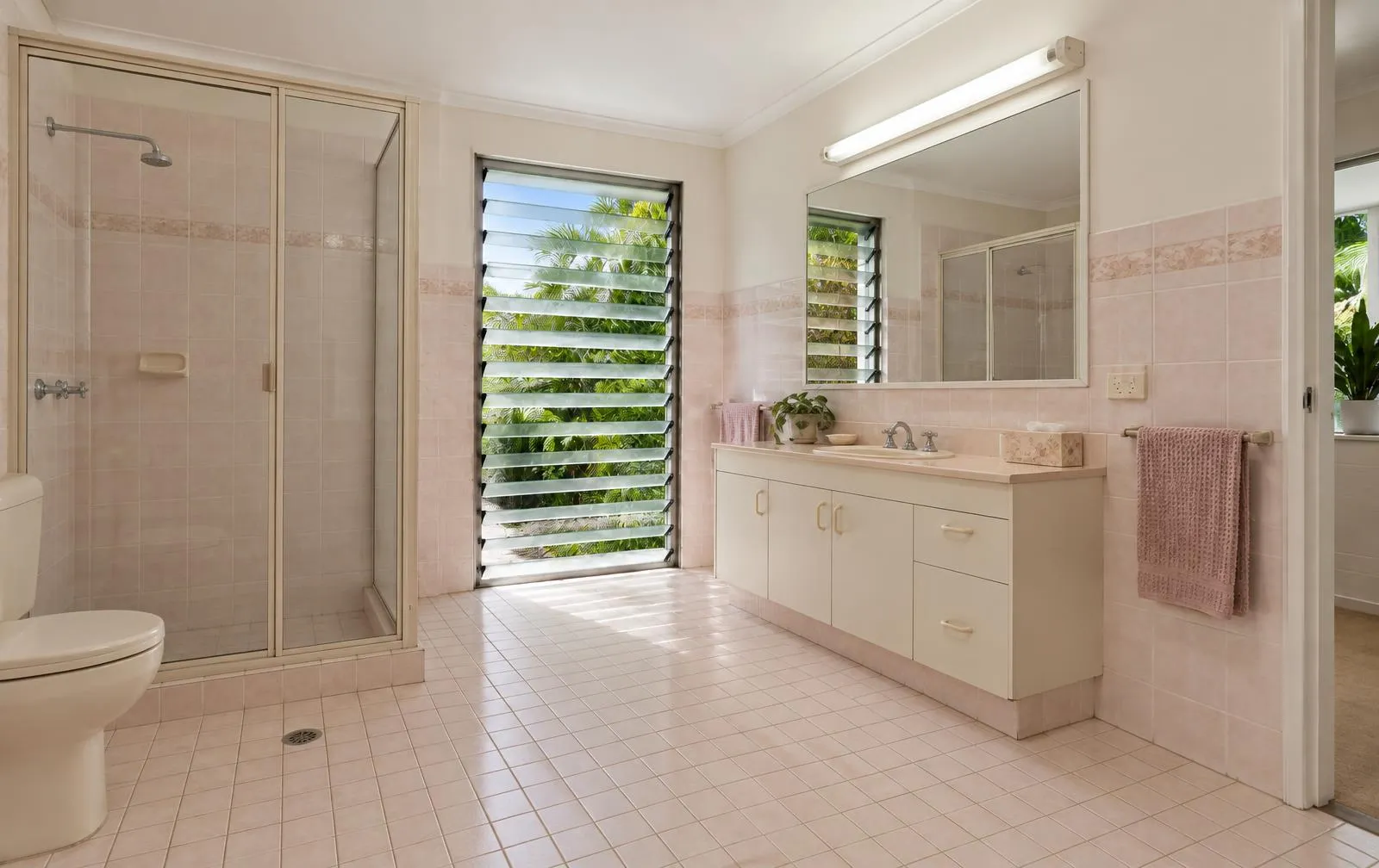 Illustrative dated 1990s bathroom with pink tiles and framed shower before renovation
